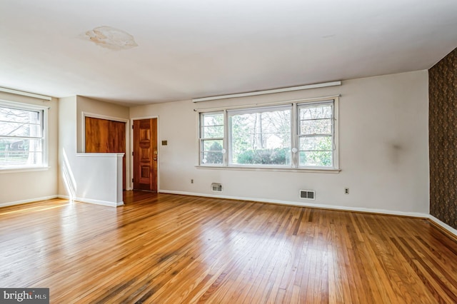 unfurnished living room with light wood-type flooring, visible vents, and baseboards