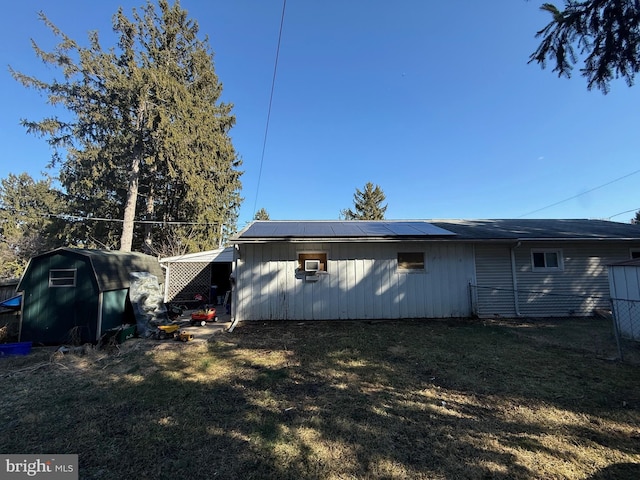 rear view of property with roof mounted solar panels, a lawn, a storage shed, and an outdoor structure