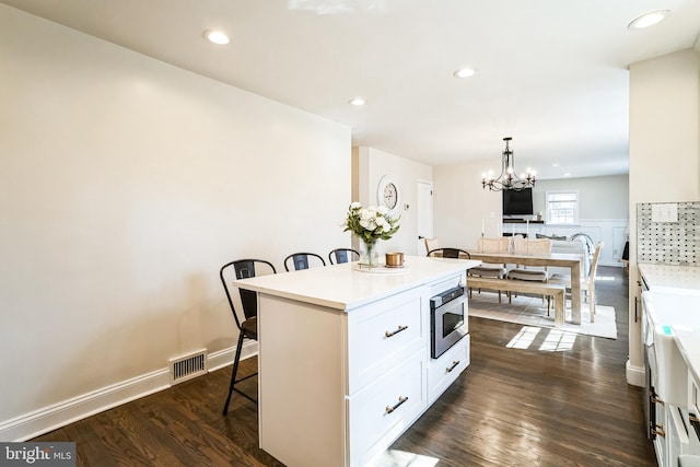 kitchen with a kitchen bar, visible vents, stainless steel microwave, dark wood finished floors, and white cabinetry