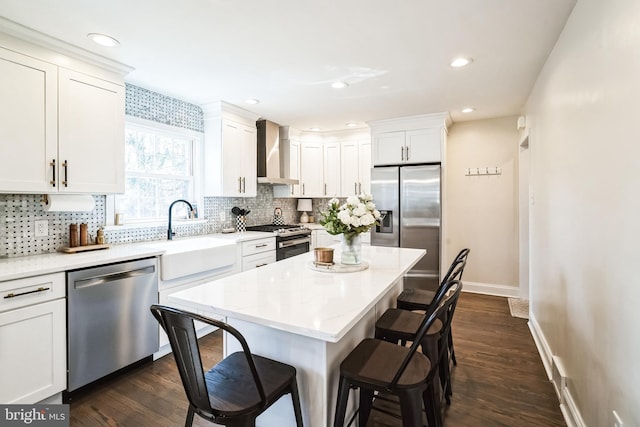 kitchen featuring wall chimney range hood, a breakfast bar, appliances with stainless steel finishes, white cabinets, and a sink