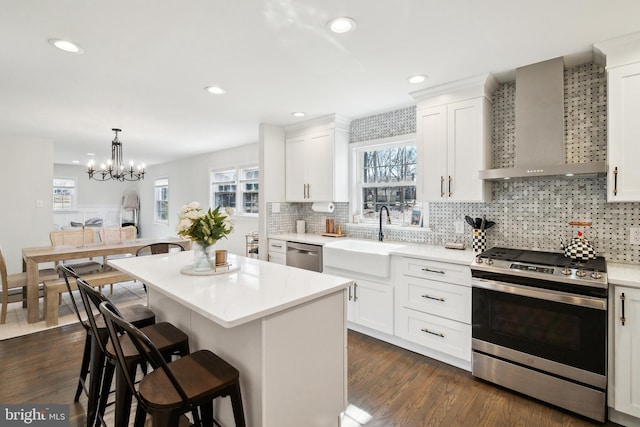 kitchen featuring a center island, a breakfast bar, appliances with stainless steel finishes, wall chimney exhaust hood, and a sink