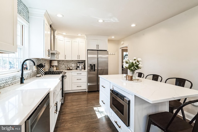 kitchen featuring dark wood finished floors, a breakfast bar area, light stone counters, decorative backsplash, and stainless steel appliances