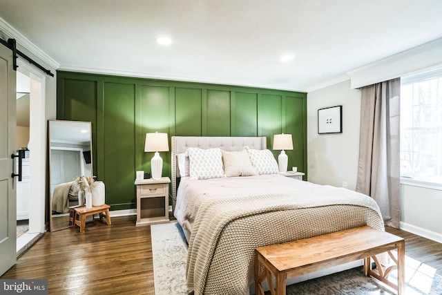 bedroom featuring dark wood finished floors, a barn door, a decorative wall, and ornamental molding