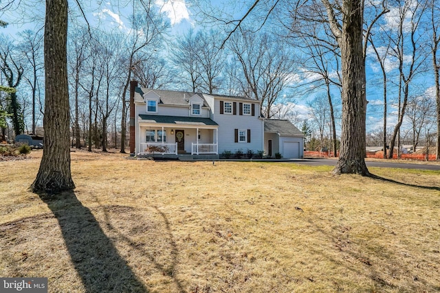 view of front facade with a front yard, covered porch, a chimney, driveway, and an attached garage