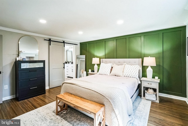 bedroom featuring a barn door, dark wood-type flooring, crown molding, and a decorative wall