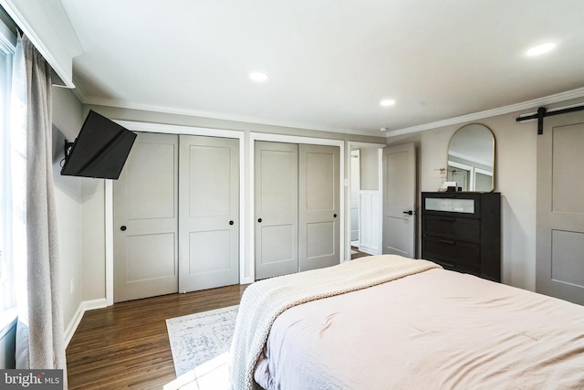 bedroom featuring two closets, ornamental molding, wood finished floors, recessed lighting, and a barn door