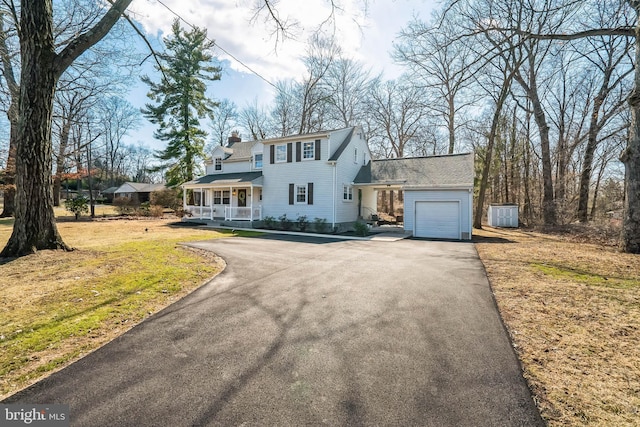 view of front of property with aphalt driveway, a porch, a front yard, an attached garage, and a chimney