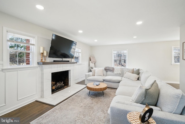 living room with a wealth of natural light, a decorative wall, a tiled fireplace, and wood finished floors