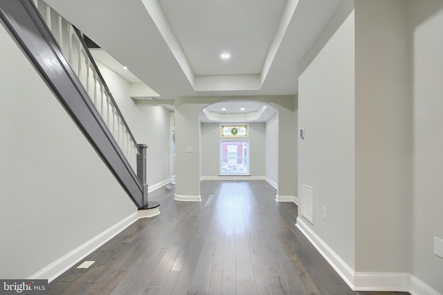 entryway with visible vents, baseboards, dark wood finished floors, a tray ceiling, and arched walkways