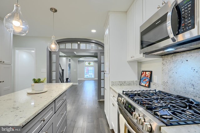 kitchen with tasteful backsplash, dark wood-type flooring, light stone counters, appliances with stainless steel finishes, and arched walkways