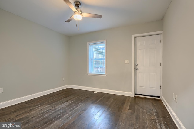 empty room with dark wood finished floors, visible vents, a ceiling fan, and baseboards