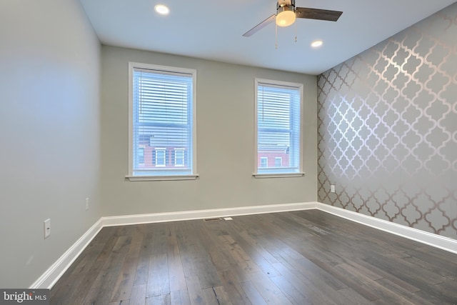 empty room with dark wood-type flooring, recessed lighting, wallpapered walls, baseboards, and an accent wall