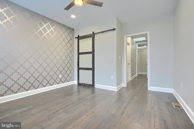 unfurnished bedroom featuring wallpapered walls, an accent wall, baseboards, a barn door, and hardwood / wood-style flooring