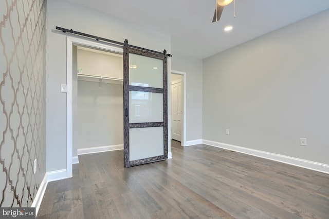 unfurnished bedroom featuring wood finished floors, baseboards, a closet, a walk in closet, and a barn door