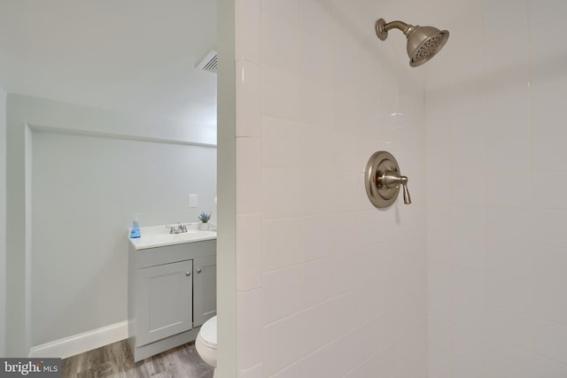 bathroom with toilet, wood finished floors, tiled shower, baseboards, and vanity