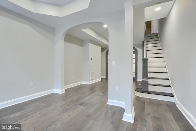 staircase with baseboards, arched walkways, visible vents, and wood-type flooring