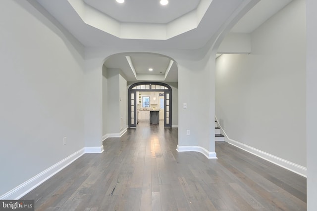 hall featuring arched walkways, dark wood finished floors, a raised ceiling, and baseboards