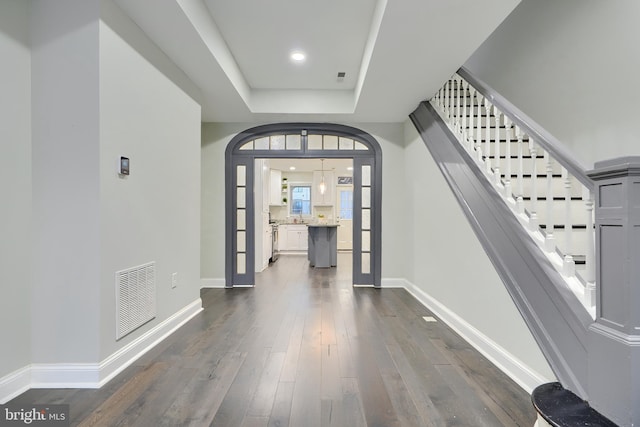 foyer with dark wood finished floors, a tray ceiling, baseboards, and visible vents