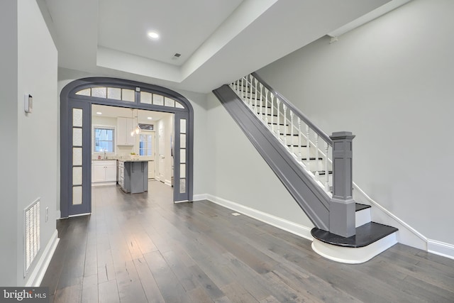 entrance foyer featuring visible vents, dark wood-style flooring, a tray ceiling, baseboards, and stairs