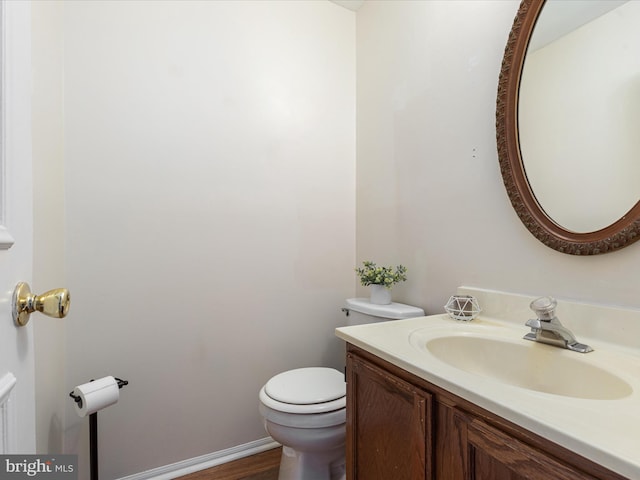 half bathroom with vanity, toilet, and baseboards