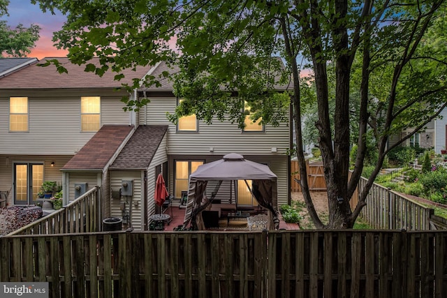 back of property at dusk featuring a gazebo, a fenced backyard, and roof with shingles