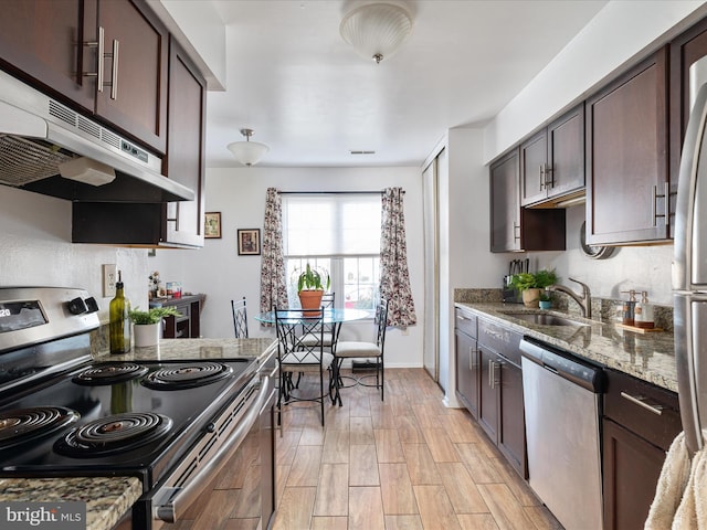 kitchen with under cabinet range hood, dark brown cabinets, appliances with stainless steel finishes, and a sink