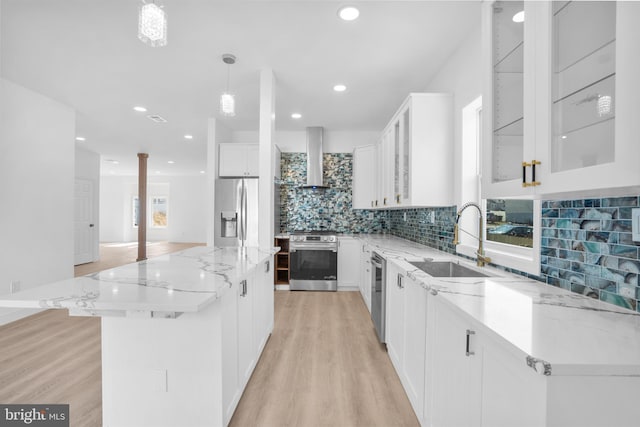 kitchen featuring light wood finished floors, a sink, appliances with stainless steel finishes, wall chimney exhaust hood, and a center island