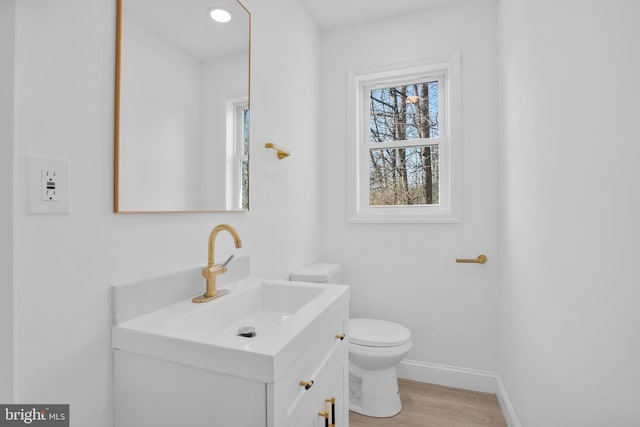 half bath with vanity, toilet, wood finished floors, and baseboards