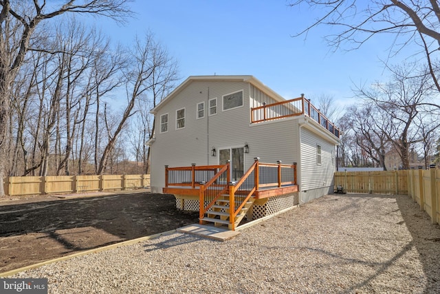 back of property with gravel driveway, a balcony, a fenced backyard, and a wooden deck