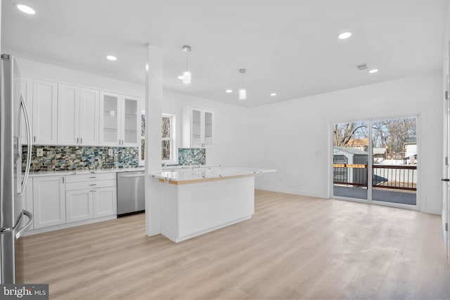 kitchen featuring light wood finished floors, a kitchen island, decorative backsplash, white cabinets, and stainless steel appliances