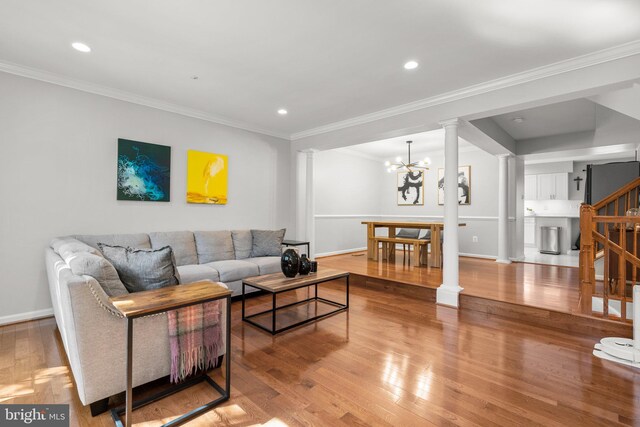 living area with baseboards, an inviting chandelier, ornamental molding, ornate columns, and wood finished floors