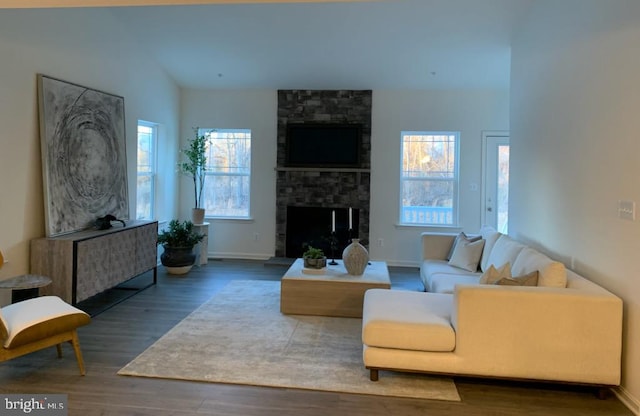 living area featuring lofted ceiling, a stone fireplace, wood finished floors, and baseboards