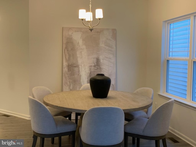 dining space with baseboards, wood finished floors, visible vents, and a notable chandelier