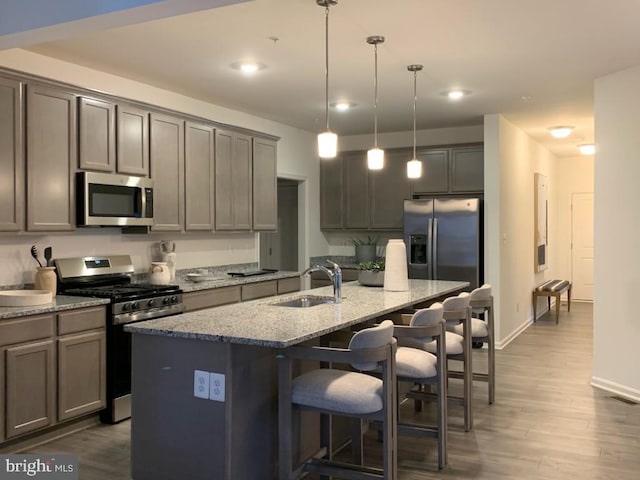 kitchen with a breakfast bar, a sink, appliances with stainless steel finishes, light stone countertops, and an island with sink