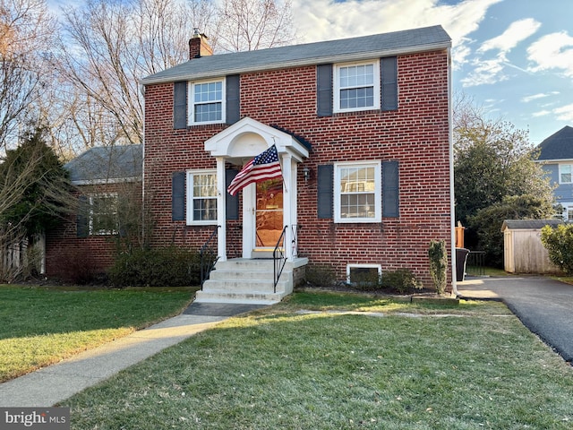 view of front of home with a front yard, brick siding, and a chimney