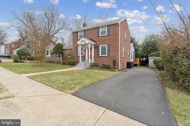 view of front of house featuring fence, driveway, a chimney, a front lawn, and brick siding