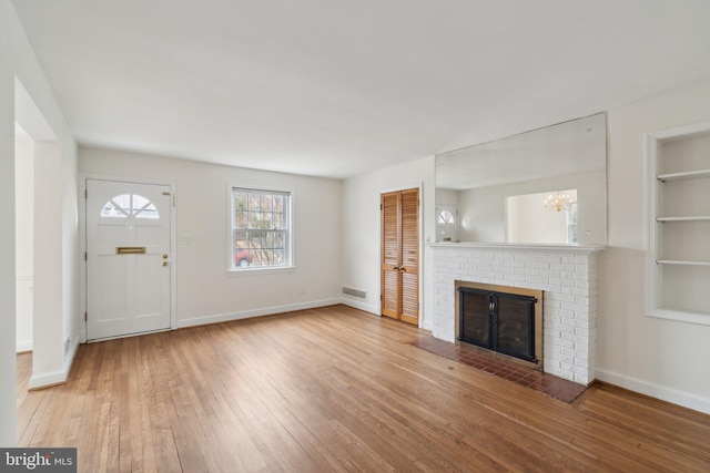 unfurnished living room featuring visible vents, hardwood / wood-style flooring, an inviting chandelier, a fireplace, and baseboards