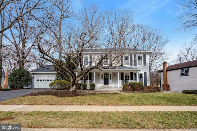 colonial-style house featuring a front yard, covered porch, driveway, and an attached garage