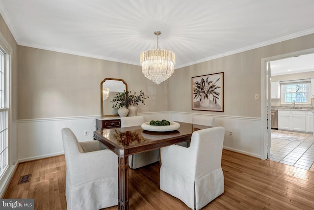 dining area featuring crown molding, visible vents, baseboards, light wood-type flooring, and an inviting chandelier