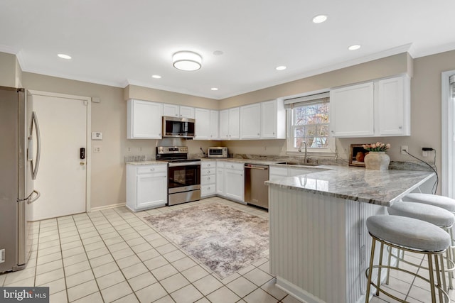 kitchen featuring stainless steel appliances, a peninsula, a sink, white cabinetry, and light stone countertops