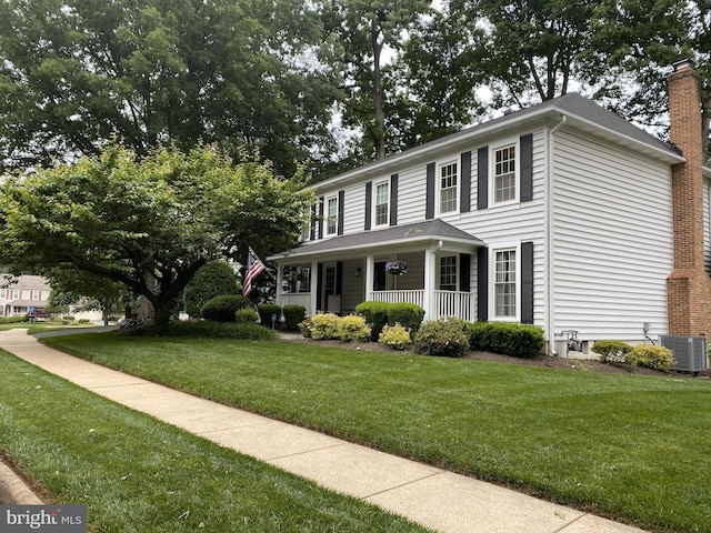 colonial inspired home with a front yard, covered porch, and a chimney