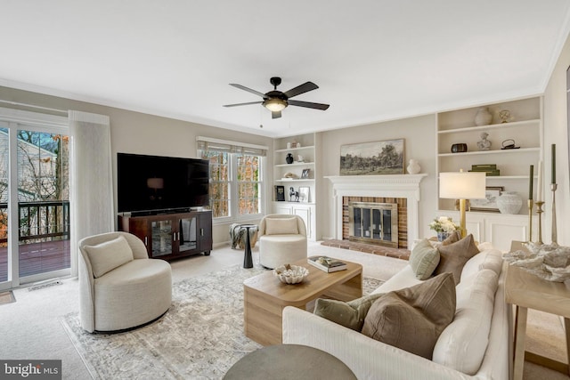 living room with built in shelves, a wealth of natural light, a brick fireplace, and carpet flooring