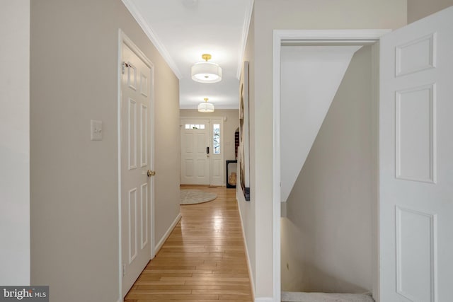 corridor with ornamental molding, light wood-style flooring, and baseboards