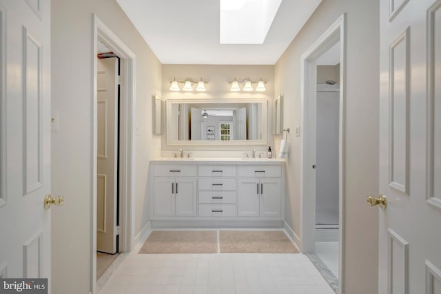 bathroom featuring double vanity, a skylight, a shower, and a sink