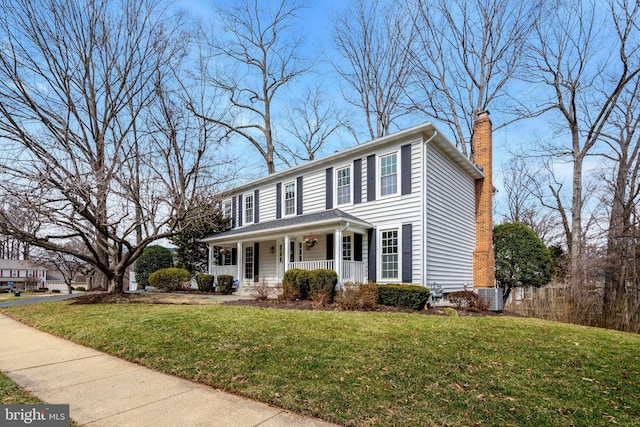 colonial house featuring covered porch, a chimney, and a front yard