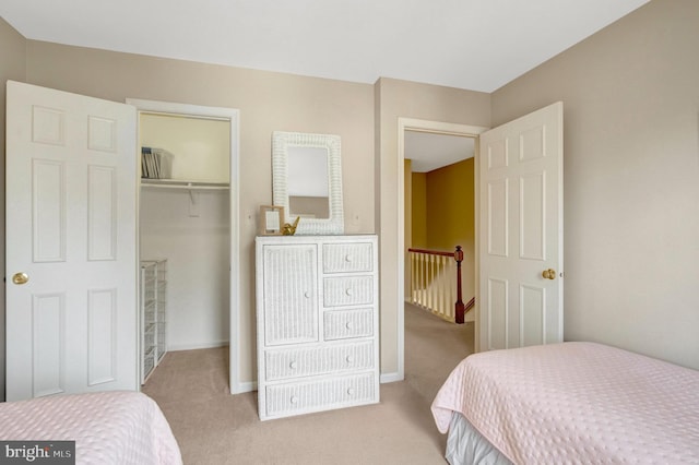 carpeted bedroom with a closet, a walk in closet, and baseboards