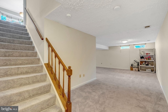 stairway with a textured ceiling, carpet floors, visible vents, and baseboards