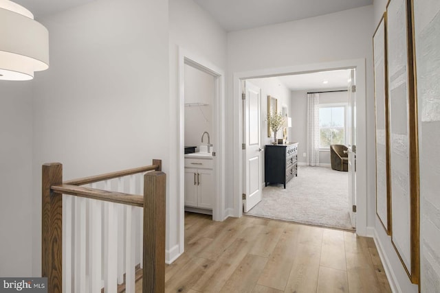 hall with baseboards, a sink, an upstairs landing, and light wood-style floors