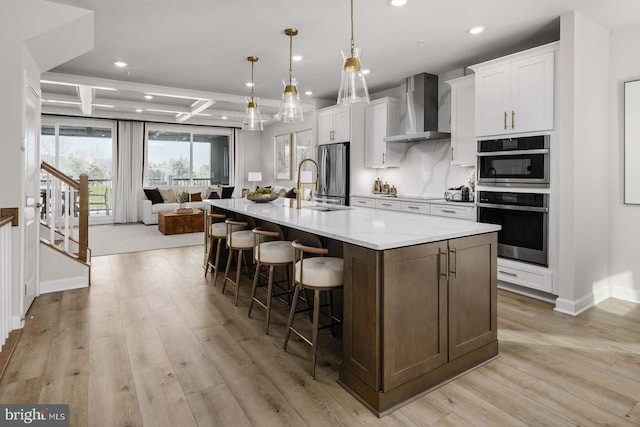 kitchen with light wood-style flooring, appliances with stainless steel finishes, a sink, wall chimney range hood, and coffered ceiling