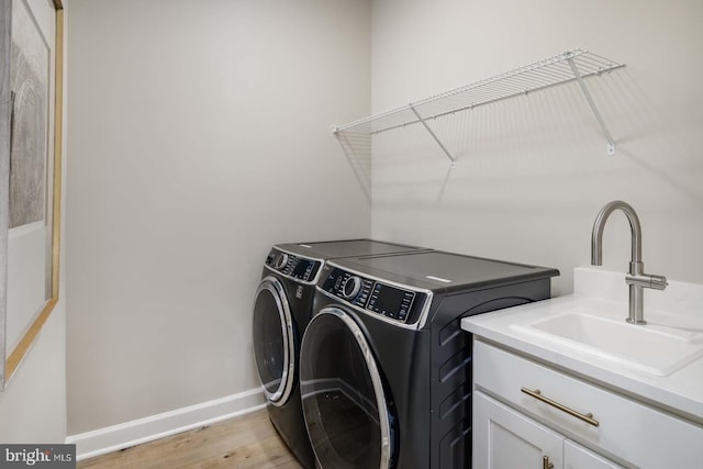 laundry room featuring cabinet space, light wood finished floors, baseboards, washing machine and clothes dryer, and a sink